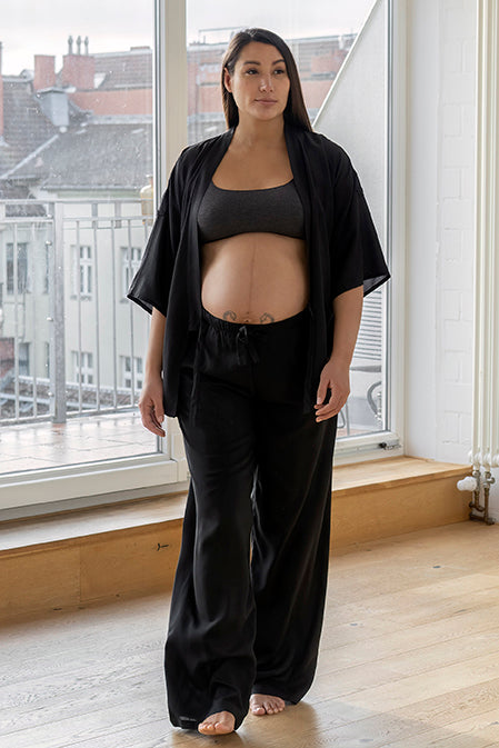 Chica embarazada camina con blusa y pantalon largo negros en viscosa de Forever 2